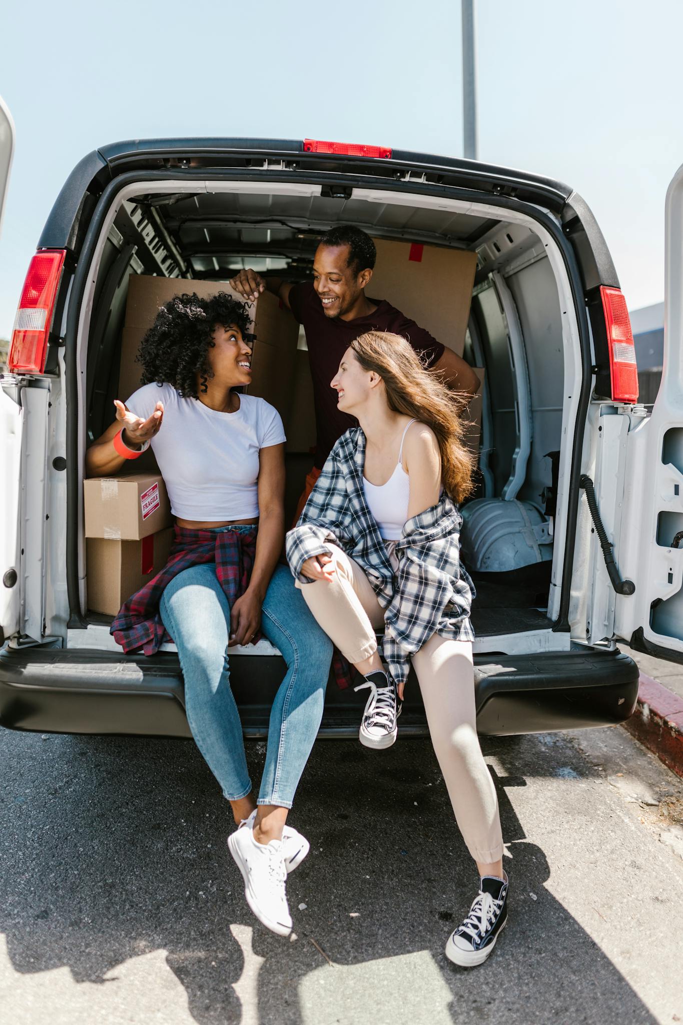 Three friends sitting on a van with moving boxes, enjoying the moving day experience.